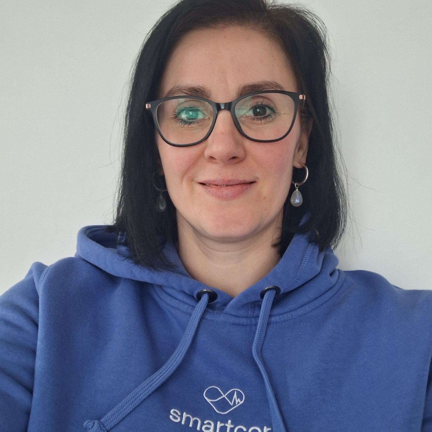 Dr._Kathrin_Borgs_Profil Foto von Dr. Kathrin Borgs; sympathische Frau mittleren Alters, mit schwarzem, schulterlangem Haar, Brille und blauem smartcor-Hoodie